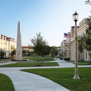 Exterior of the Greek Village at TCU, where a tall obelisk monument bearing greek letters is surrounded group of sorority and fraternity houses 